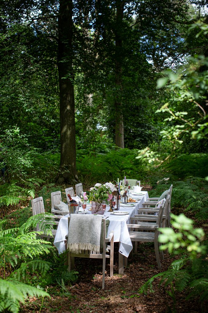 Outdoor dining setup in a forest clearing near Solihull, with a long table dressed in white linen