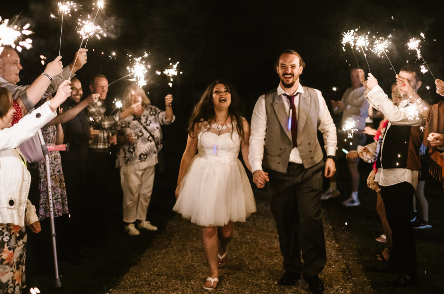 Bride and groom walking through a sparkler tunnel surrounded by guests, capturing joyful moments at weddings at Stone Manor.