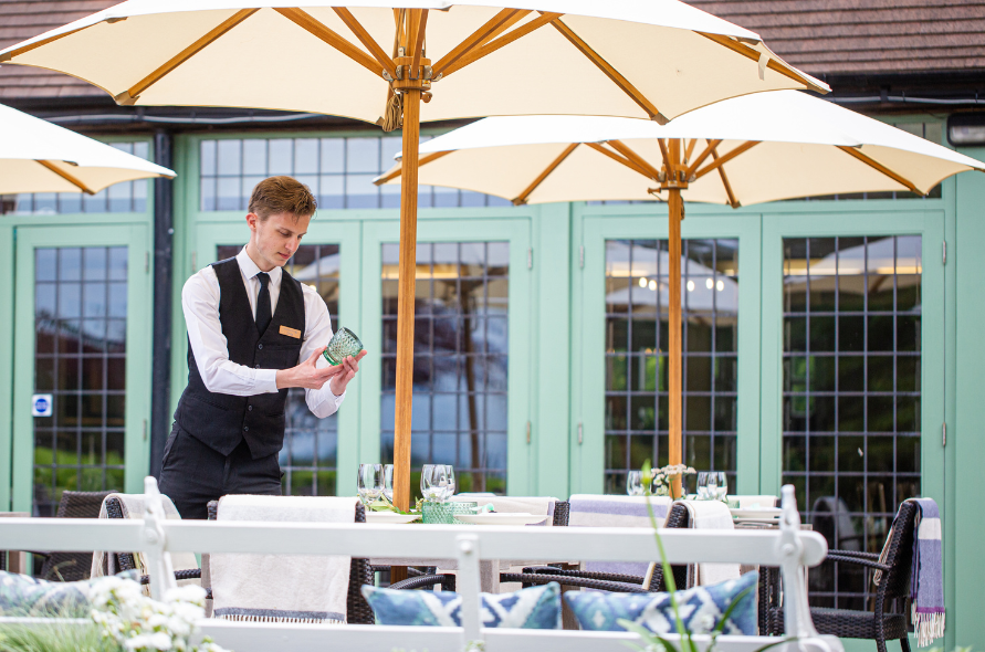 Waiter serving drinks under parasols in a courtyard, part of outdoor hospitality for weddings at Stone Manor.