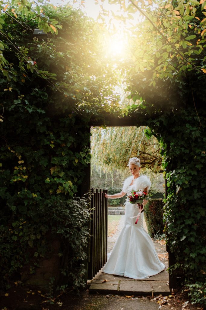 Bride posing in a romantic ivy-covered garden archway at sunset, capturing a magical moment during weddings at Stone Manor.