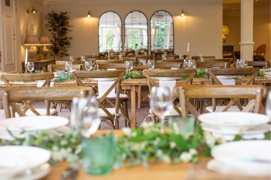 Indoor wedding reception setup with long wooden tables and greenery, offering a beautiful rustic venue for weddings at Stone Manor.
