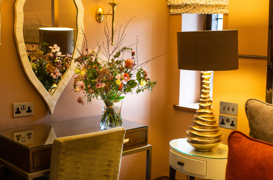 Dressing table with floral arrangement and mirror in a warmly lit room at Stone Manor, ideal for bridal prep.