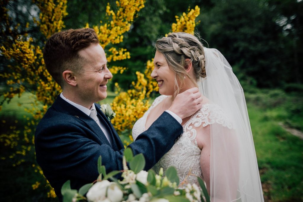 Newlyweds sharing an intimate moment in the gardens of Stone Manor, with greenery and vibrant blooms in the background.