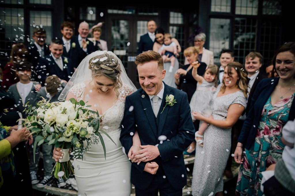 Bride and groom laughing with their guests during a joyful confetti moment outside the venue, part of weddings at Stone Manor.