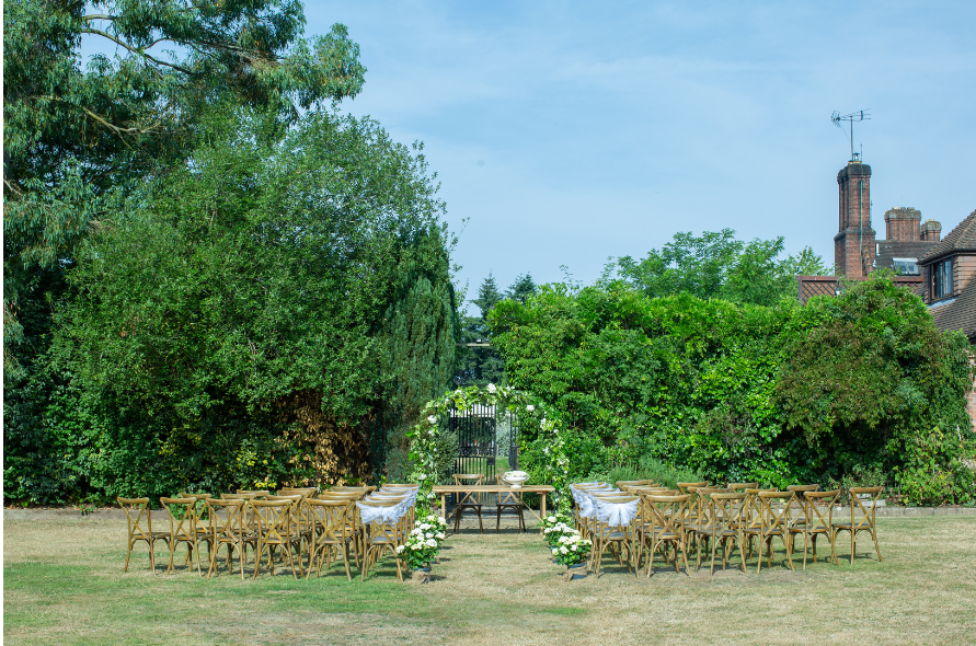 Intimate outdoor ceremony space with wooden chairs and a rustic arch surrounded by lush greenery for weddings at Stone Manor.