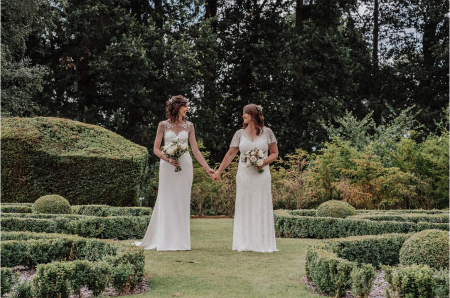 Two brides walking hand-in-hand through the beautifully landscaped gardens, celebrating weddings at Stone Manor.