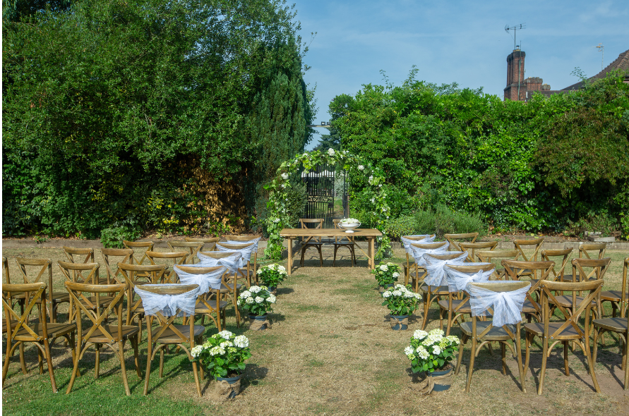 Garden ceremony arrangement with wooden chairs and floral decorations, set against the backdrop of historic architecture at Stone Manor weddings.