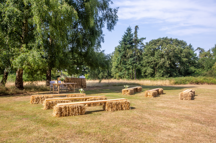Rustic outdoor wedding setting at Stone Manor featuring hay bale seating under a large tree in a natural meadow.