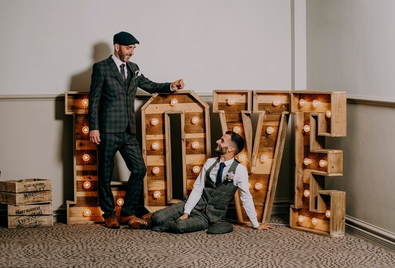 Playful wedding photo of grooms in front of large illuminated LOVE letters during a Stone Manor celebration.