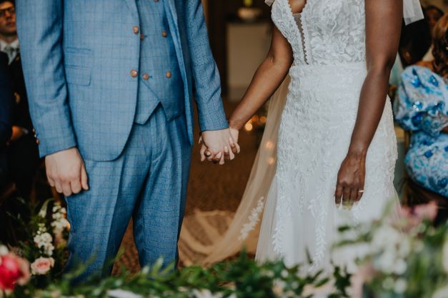 Close-up of newlyweds holding hands during their wedding vows at Stone Manor, dressed in elegant attire