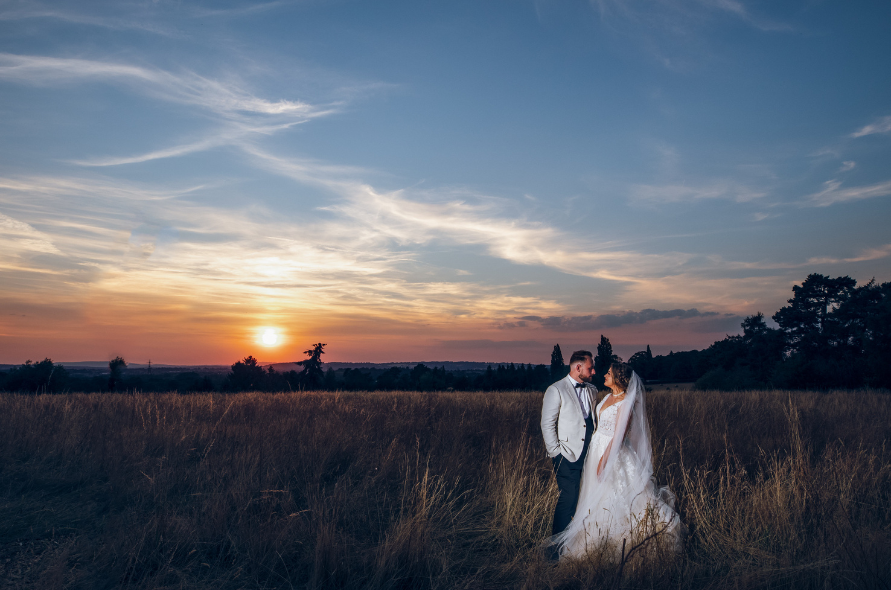 Bride and groom walking hand-in-hand through a golden field at sunset, capturing a romantic wedding moment at Stone Manor.