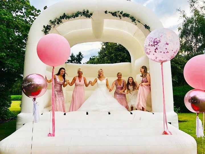 Bridal party in pink dresses celebrating on a white wedding bouncy castle at Stone Manor gardens.