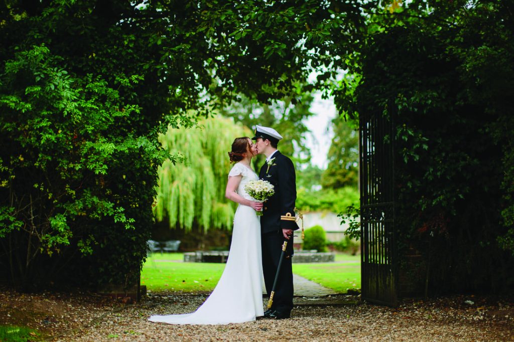 Bride and groom sharing a romantic moment framed by greenery at Stone Manor's picturesque garden entrance.