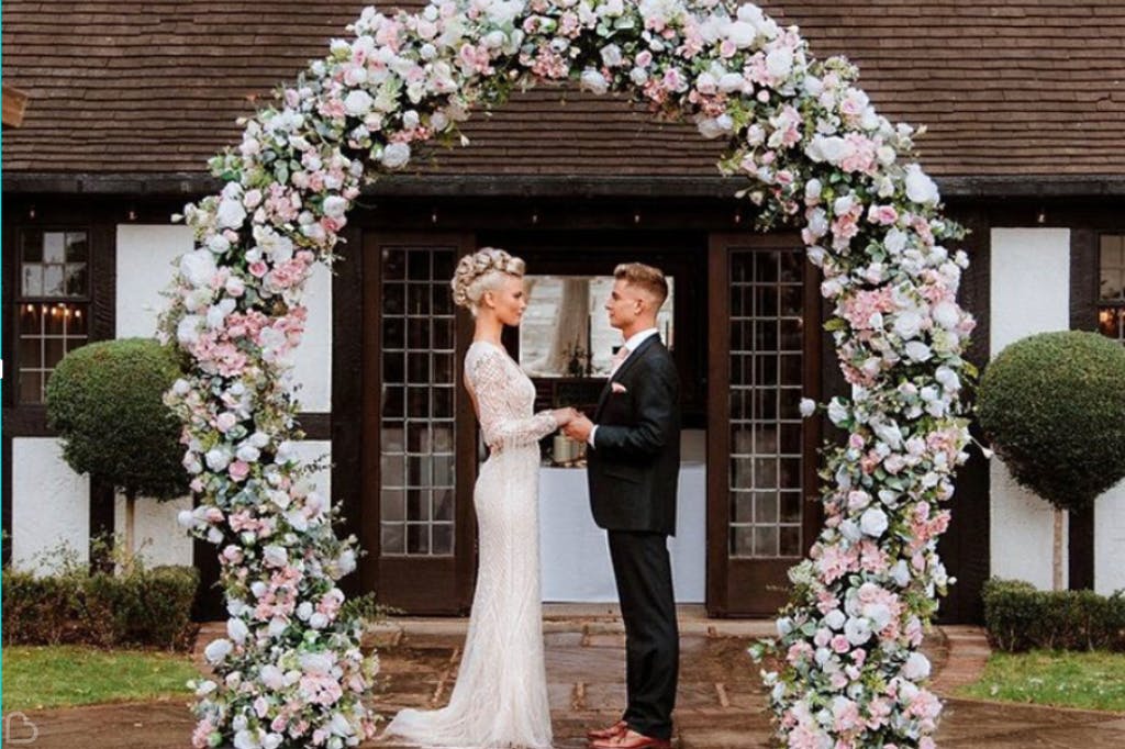 Bride and groom standing under a flower arch, captured during their wedding ceremony at Stone Manor.